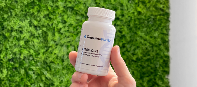 Hand holding a GenuinePurity™ Spermidine product bottle with a green grass wall background