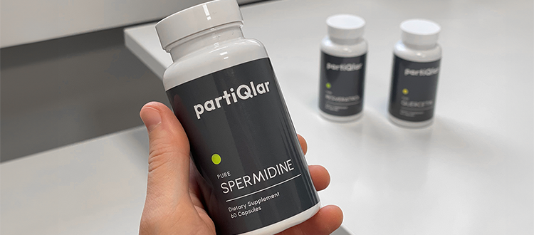 Hand holding a partiQlar Spermidine product bottle, two other supplement bottles in the background