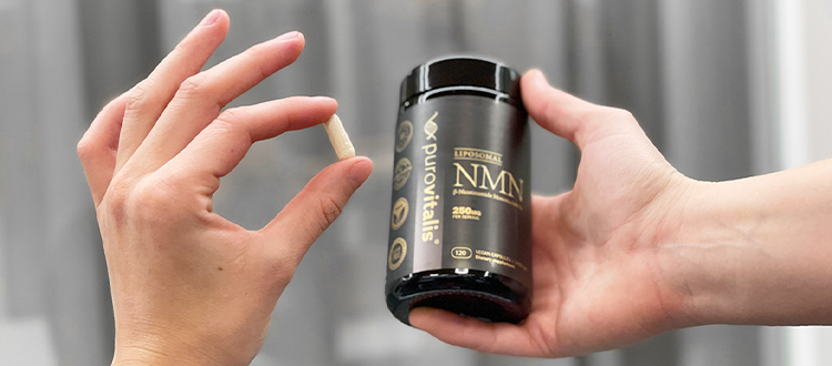 Hand holding Purovitalis Liposomal NMN bottle and its pill in other hand grey background
