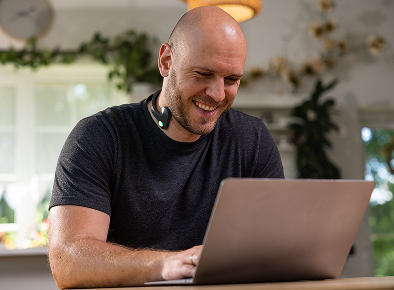 Person using a Pulsetto device while working on a computer in a home office setting