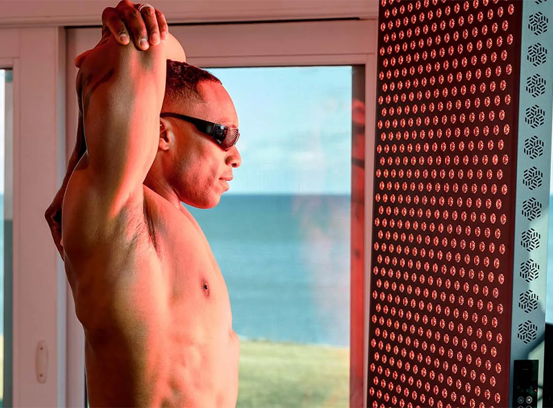 Person stretching in front of a Hooga Ultra1500 Red Light Therapy Device