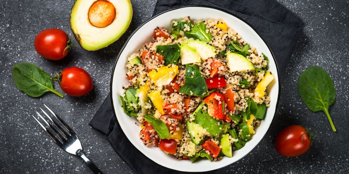 Quinoa salad with spinach, avocado, paprika and tomatoes on black stone table