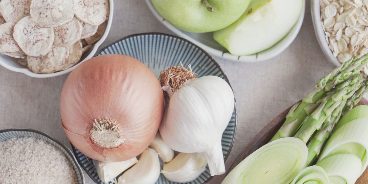 An onion, garlic, asparagus, apple, and oats on a white table