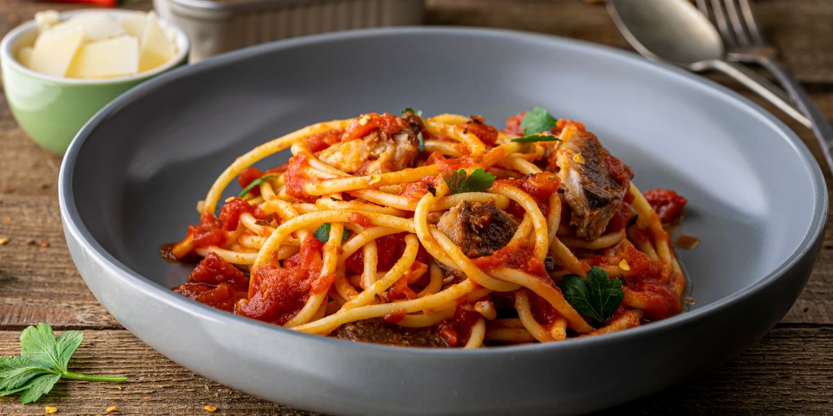 A bowl of Italian bucatini pasta with tomato sauce and sardine on the table