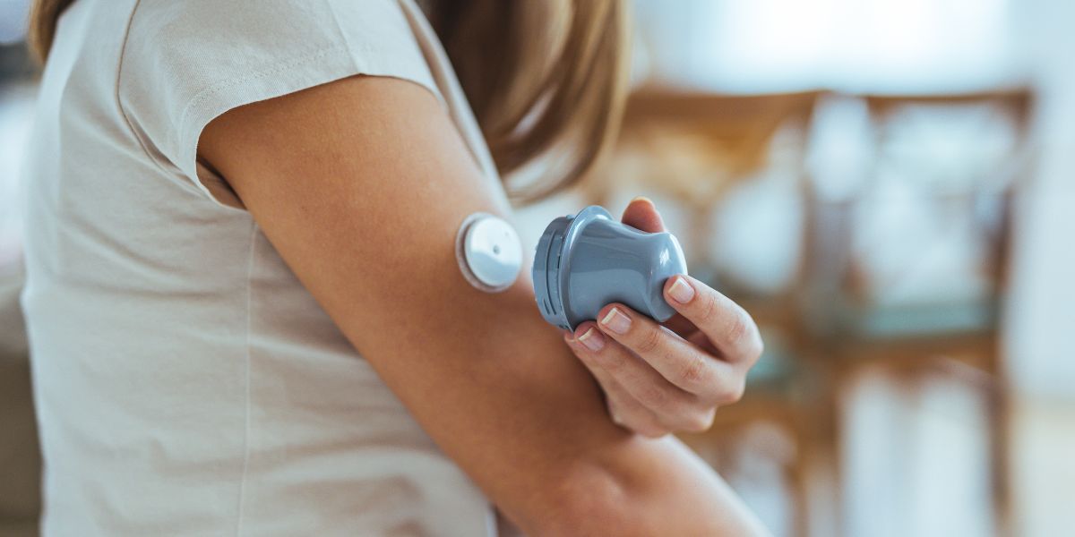 A woman applies a glucose monitor sensor to her arm.
