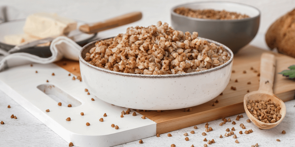 Board with bowl of tasty buckwheat porridge on white table