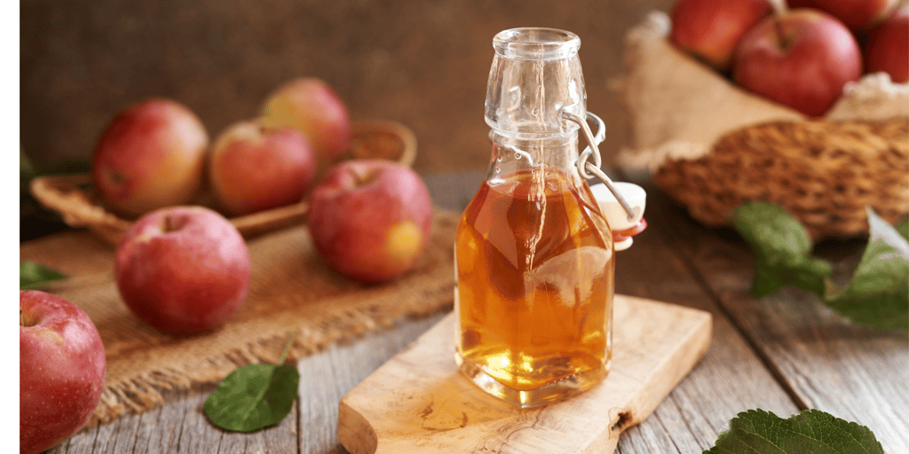A glass bottle containing apple cider vinegar and apples on the table.