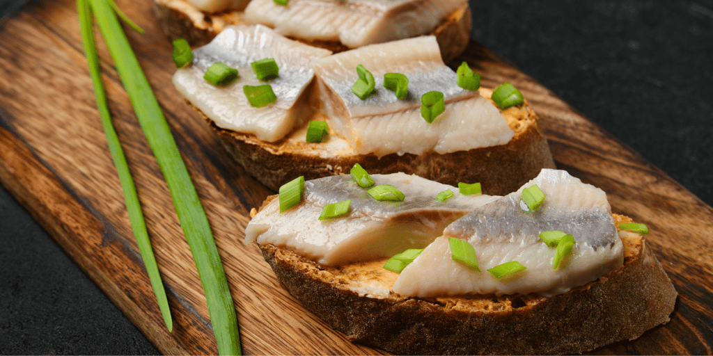 Sandwiches with salty herring and spring onion on the brown board
