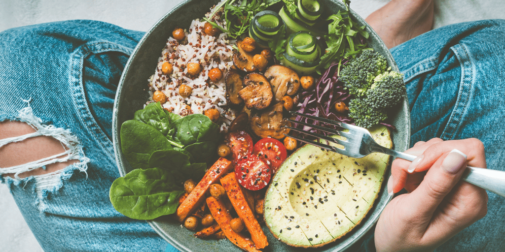Woman eating healthy meal. Bowl with rice, quinoa, avocado, cucumber, broccoli and cucumber.