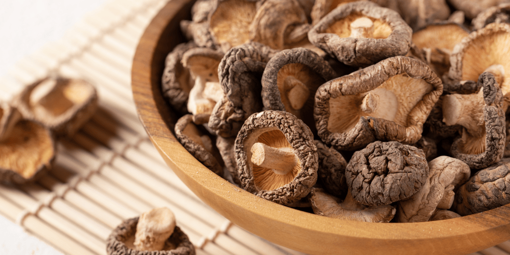 Dried shiitake mushrooms closeup in a wooden bowl on a bamboo mat.