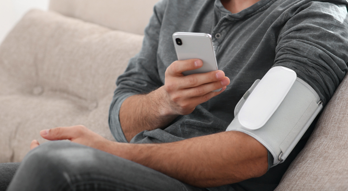 Man checking blood pressure with modern monitor and smartphone