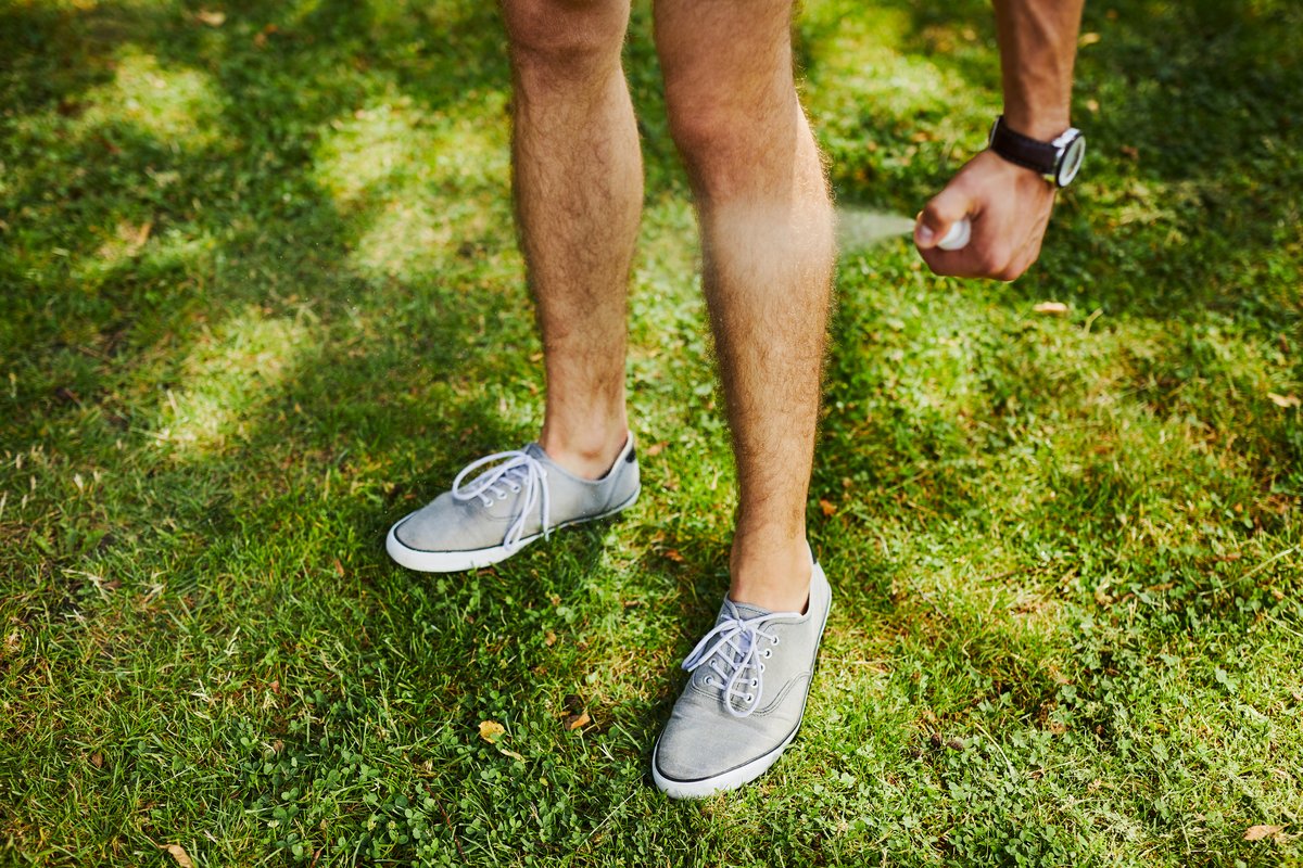 Man using spray bottle of insect repellent on his leg outdoors.
