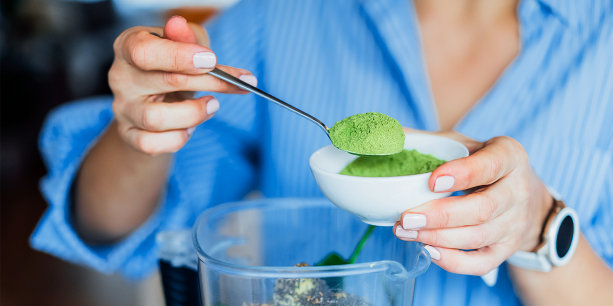 Woman adding green powder supplement to blender