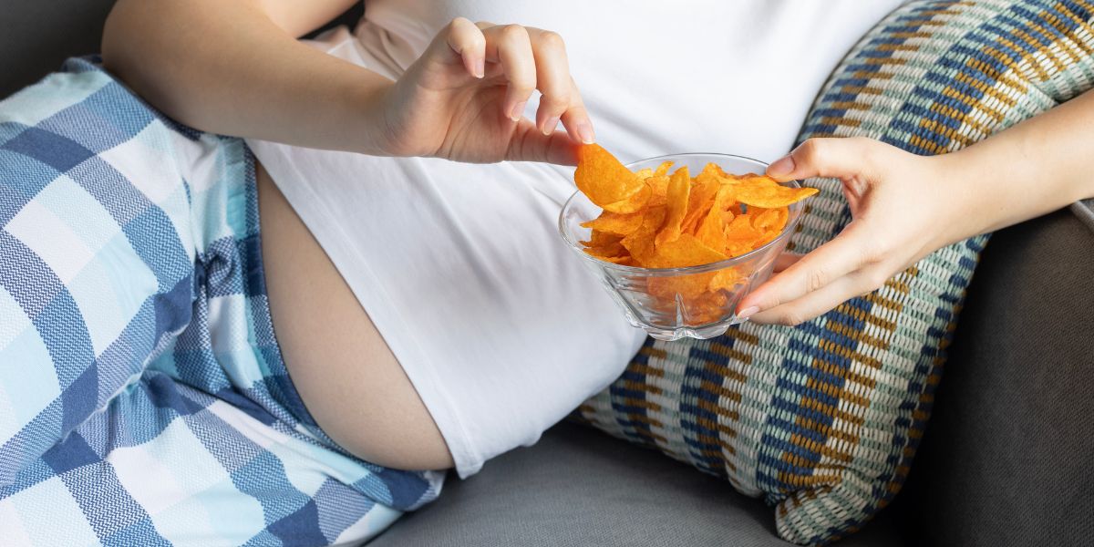 Pregnant woman on a couch holding a bowl of orange potato chips