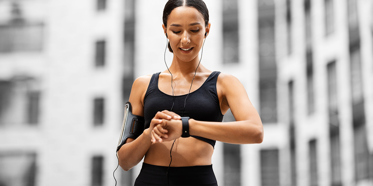 Person in gym attire checks the fitness tracker on their arm, grey buildings in the background