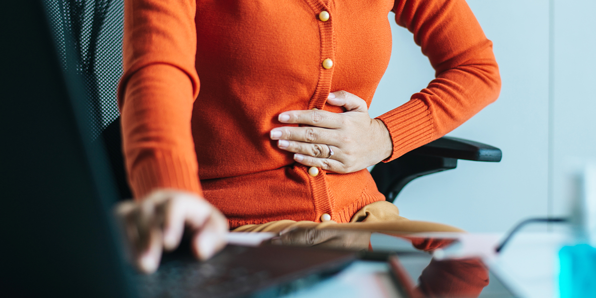Person sitting behind desk feeling their stomach for discomfort