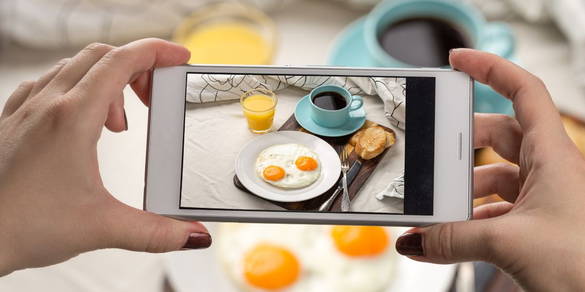 Person using smartphone to take photos of eggs, coffee, toast, and orange juice