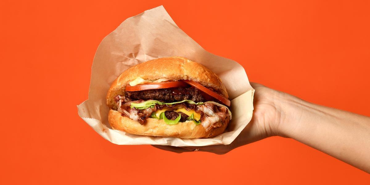 A hand holding a bacon cheeseburger with lots of toppings