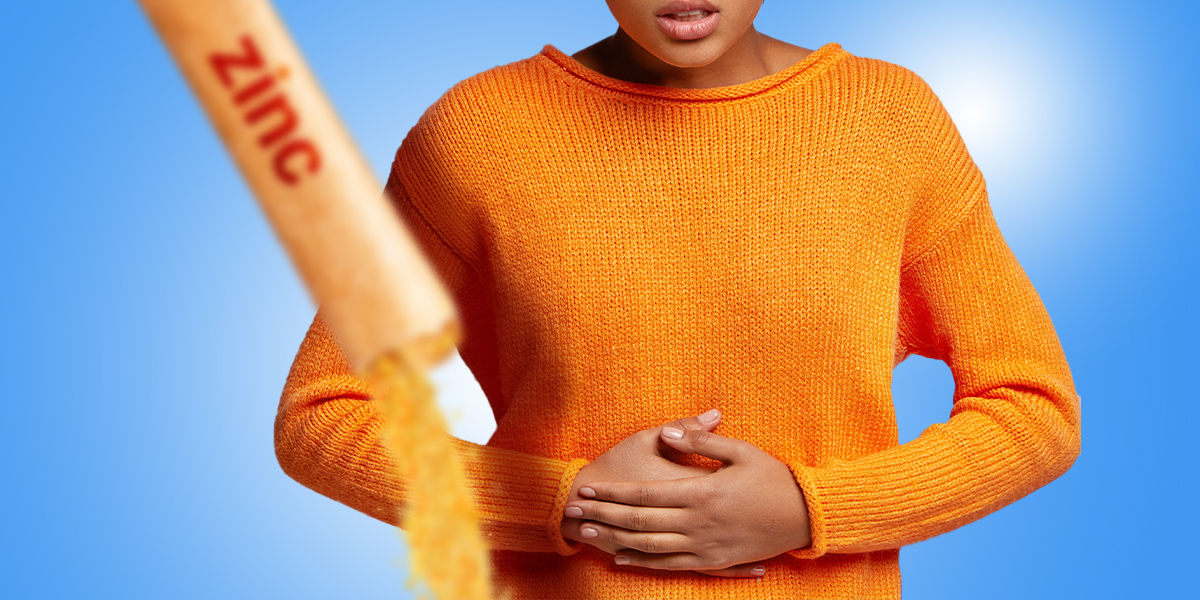 Zinc supplements spilling from a packet, person holding onto their stomach in the background