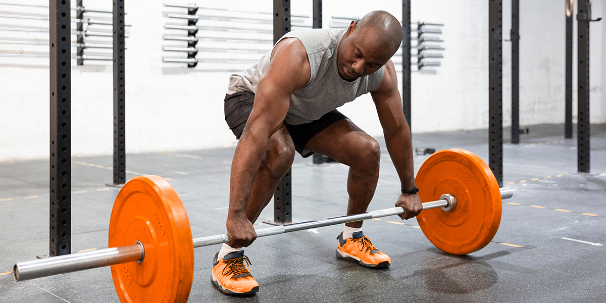 Dark skin person preparing to deadlift orange bar