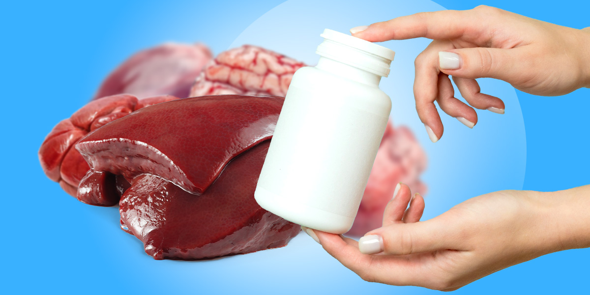 A hand holding a bottle supplements with organ meat in the background