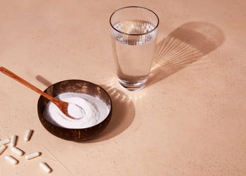 Collagen protein powder capsules and glass of water on a beige background