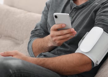 Man checking blood pressure with modern monitor and smartphone