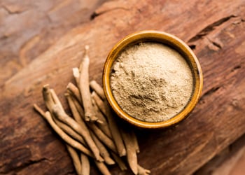Ashwagandha root and powder on a dark wooden table in a wooden bowl