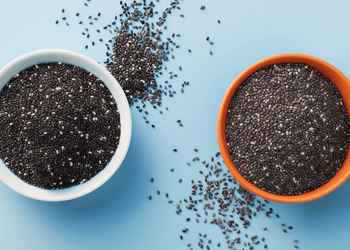 Spilled basil and chia seeds in white and orange bowls on a blue table