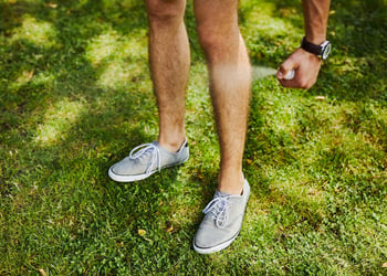 Man using spray bottle of insect repellent on his leg outdoors.