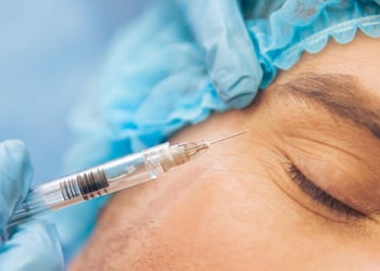 Portrait of a person receiving a face injection, lying down with eyes closed