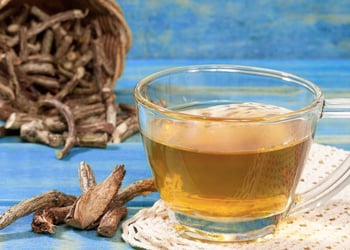 Transparent cup of valerian tea with valerian root on the side, set on a blue table