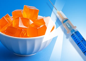 A small bowl of gelatin cubes and a syringe on the blue bakcground