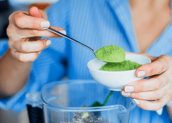 Woman adding green powder supplement to blender