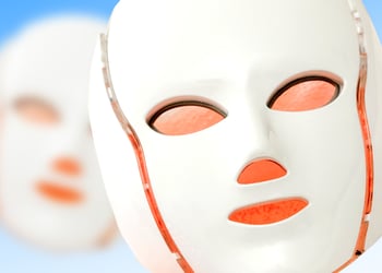 Two red light therapy masks set against a blue background