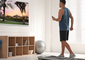 Man using a walking pad in his living room while watching tv