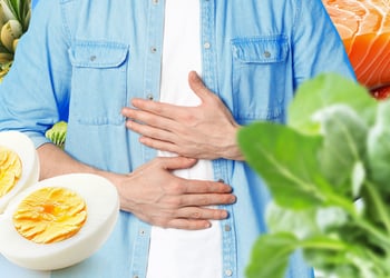 Torso feeling their stomach with variety of foods around them: eggs, pineapple, salmon