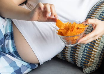 Pregnant woman on a couch holding a bowl of orange potato chips
