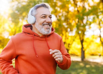 happy older man wearing orange sweatshirt jogging outdoors