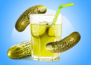 A glass of pickle juice surrounded my pickles with a blue background