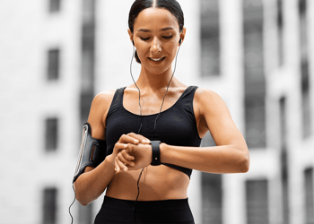 Person in gym attire checks the fitness tracker on their arm, grey buildings in the background