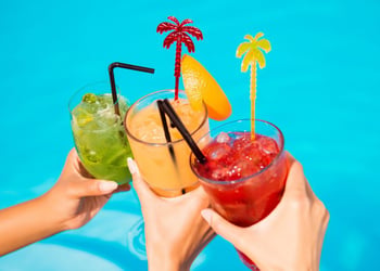 Three hands holding colorful alcoholic beverages over blue background