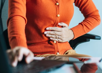 Person sitting behind desk feeling their stomach for discomfort
