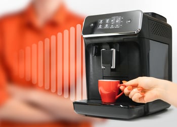 A person's hand holding a cup next to a coffee machine
