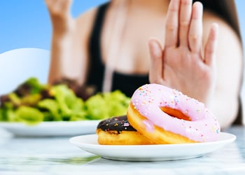 Person behind the table saying no to donuts with a healthy plate in background