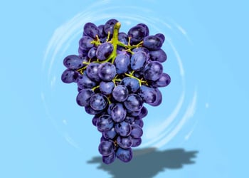 Purple grapes floating on a light blue background