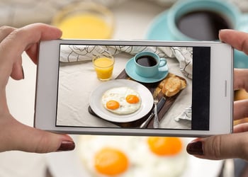 Person using smartphone to take photos of eggs, coffee, toast, and orange juice
