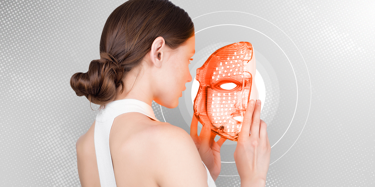 Person putting a led light therapy mask, set against grey background