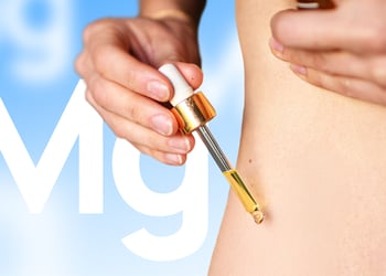 A person holding a dropper of magnesium oil up to the stomach