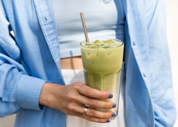A hand holding an iced matcha latte